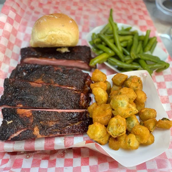 Smoked ribs with a bun, fried okra, and green beans served on red and white checkered paper.