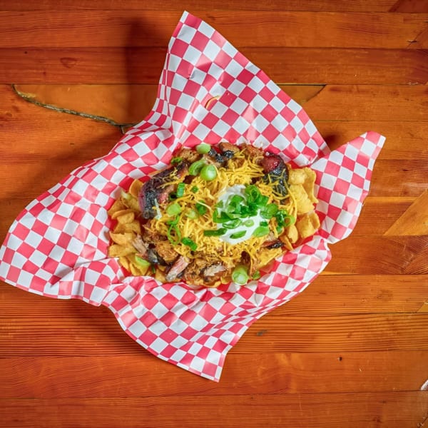 Nachos with pulled pork, shredded cheese, sour cream, and green onions in a red and white checkered basket.