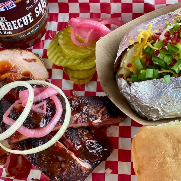 Al's Smokehouse BBQ ribs, turkey, loaded baked potato, pickles, and a roll on a red checkered tray.