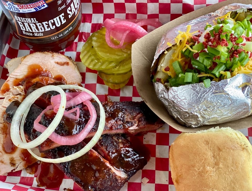 Al's Smokehouse BBQ ribs, turkey, loaded baked potato, pickles, and a roll on a red checkered tray.