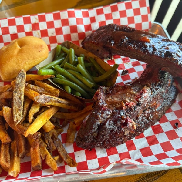 BBQ ribs with green beans, french fries, and a dinner roll on red and white checkered paper.