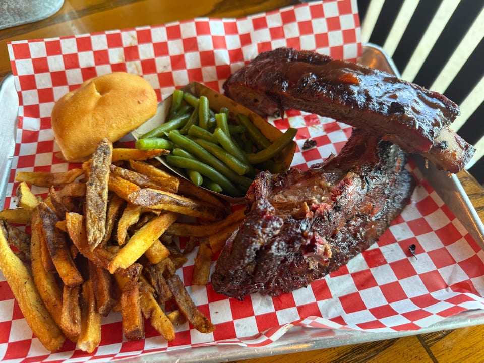 BBQ ribs with green beans, french fries, and a dinner roll on red and white checkered paper.