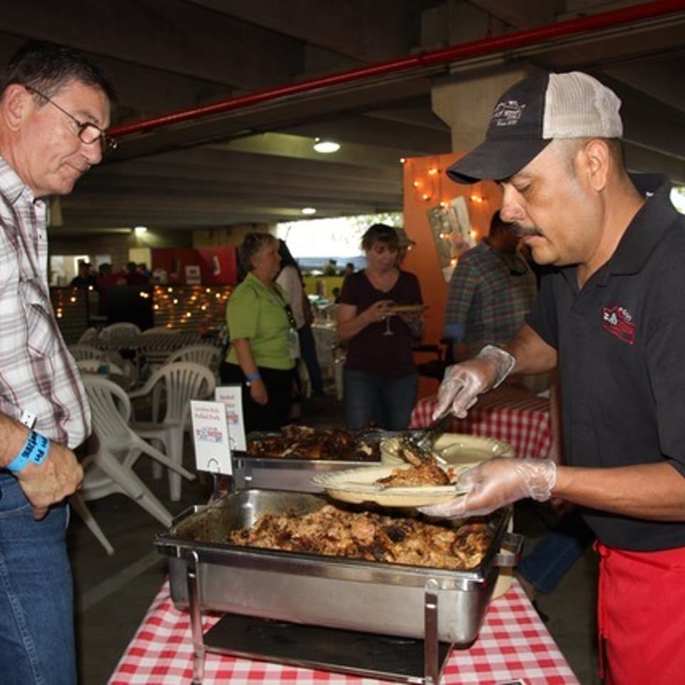 A chef serves grilled chicken from a buffet to a man in a plaid shirt at an event.