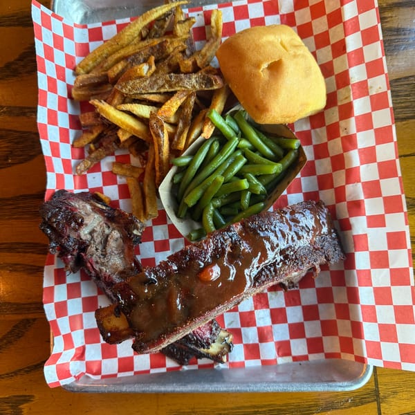 BBQ ribs with sauce, french fries, green beans, and a dinner roll on a checkered paper-lined tray.