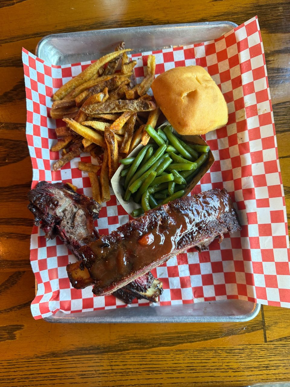 BBQ ribs with sauce, french fries, green beans, and a dinner roll on a checkered paper-lined tray.