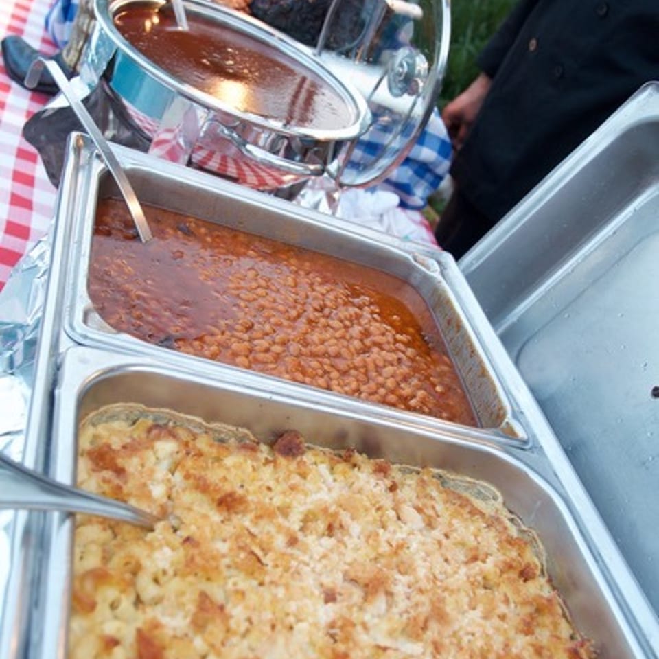 Buffet of baked beans, mac and cheese, and other dishes on a checkered tablecloth.