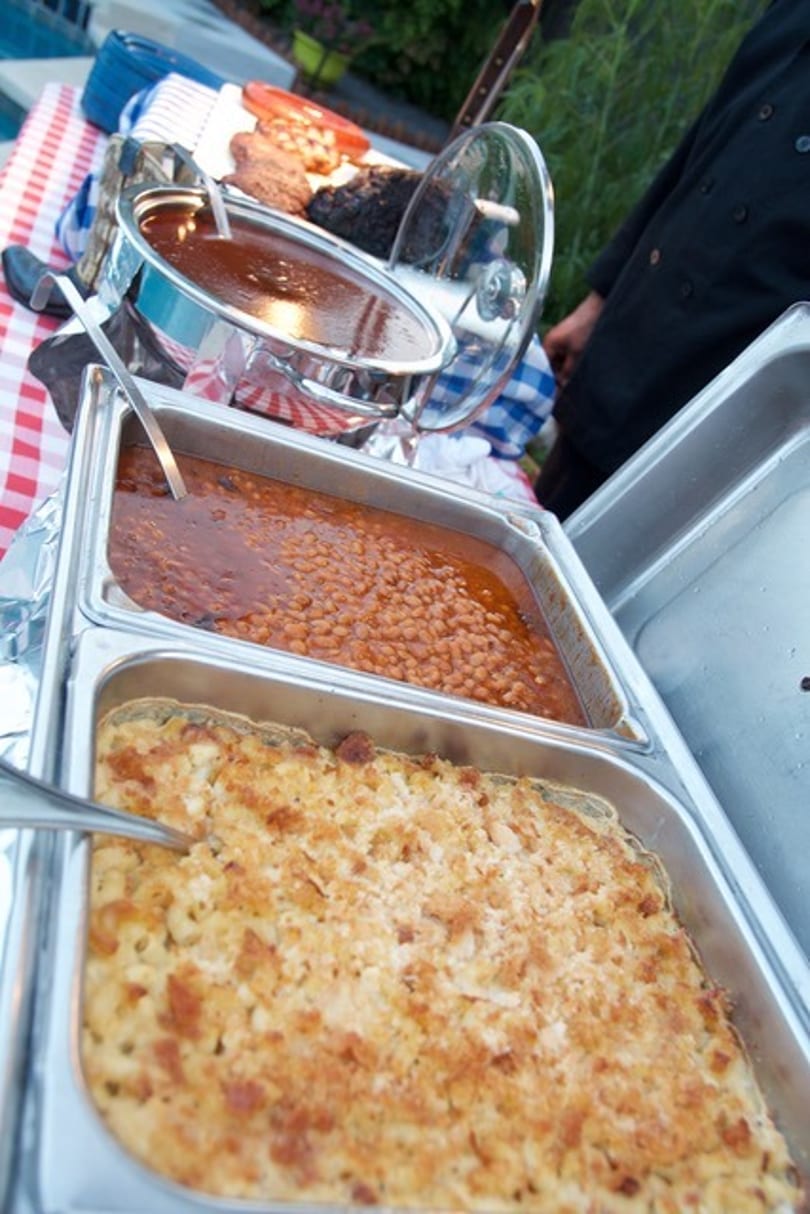 Buffet of baked beans, mac and cheese, and other dishes on a checkered tablecloth.