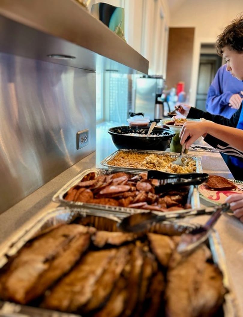 A buffet line with trays of smoked meats, macaroni and cheese, and other dishes.