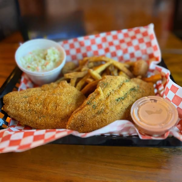 Fried fish and french fries in a basket with coleslaw and dipping sauce.