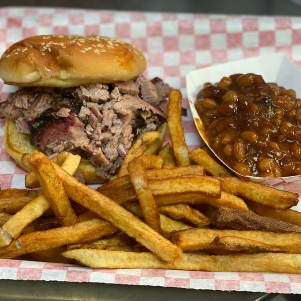 Brisket sandwich with fries and baked beans on red and white checkered paper.