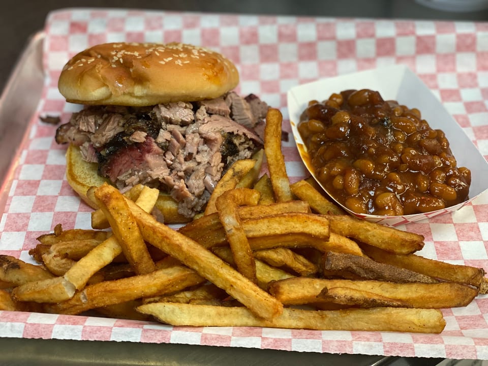 Brisket sandwich with fries and baked beans on red and white checkered paper.