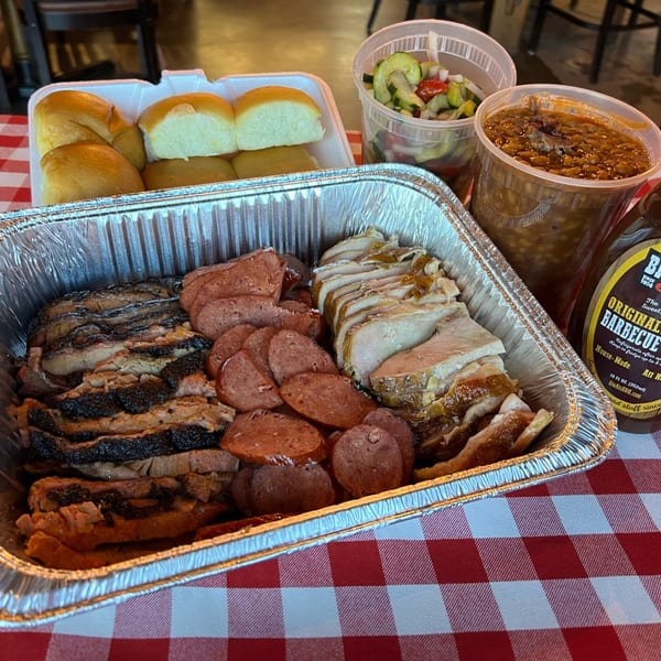 Big Al's BBQ family meal with sliced brisket, sausage, turkey, rolls, baked beans, and cucumber salad.