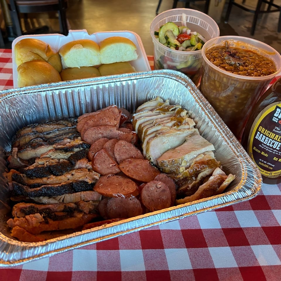 Big Al's BBQ family meal with sliced brisket, sausage, turkey, rolls, baked beans, and cucumber salad.