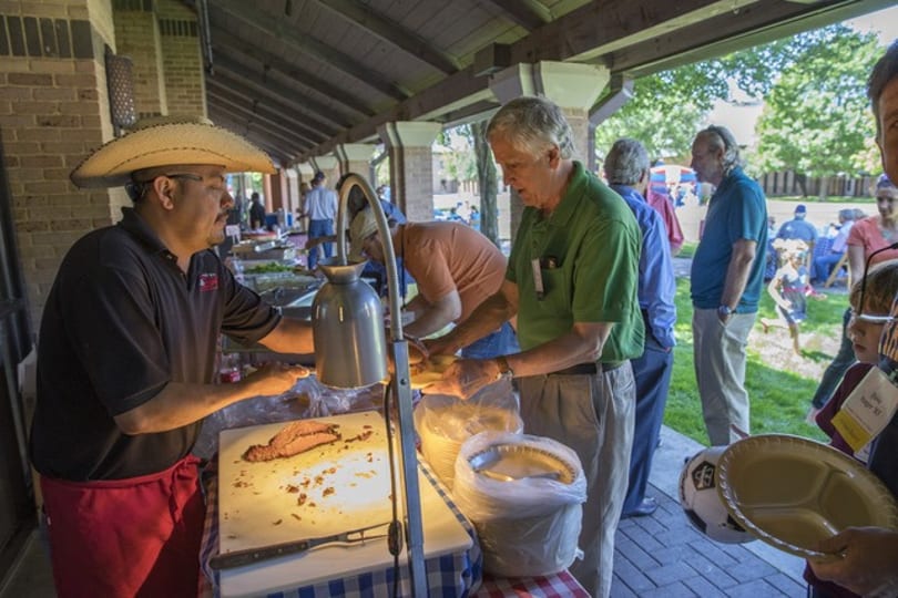 A man in a sombrero carves meat at an outdoor buffet, serving a line of people.