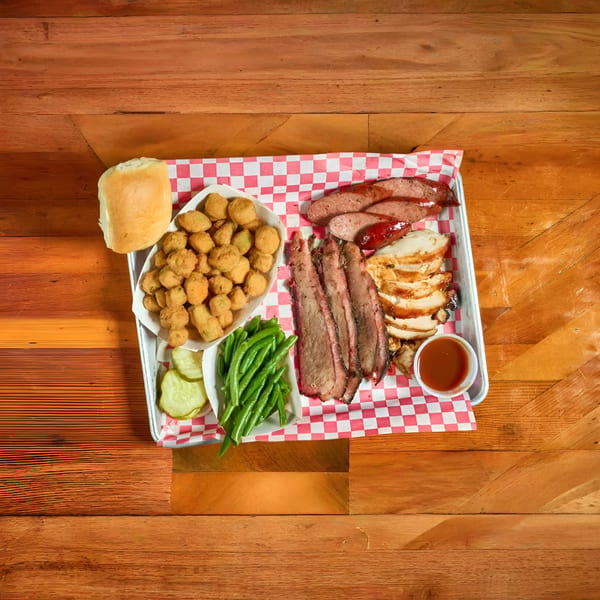 Barbecue platter with sliced brisket, chicken, sausage, fried okra, green beans, pickles, and a roll.