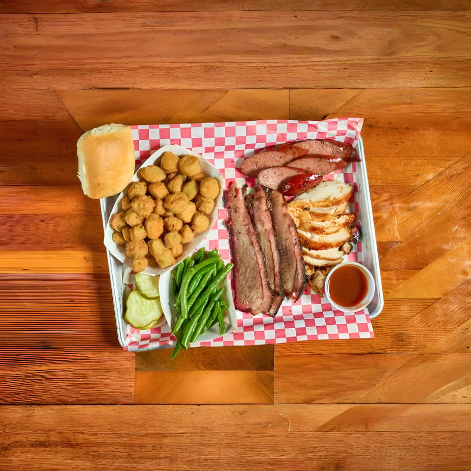 Barbecue platter with sliced brisket, chicken, sausage, fried okra, green beans, pickles, and a roll.