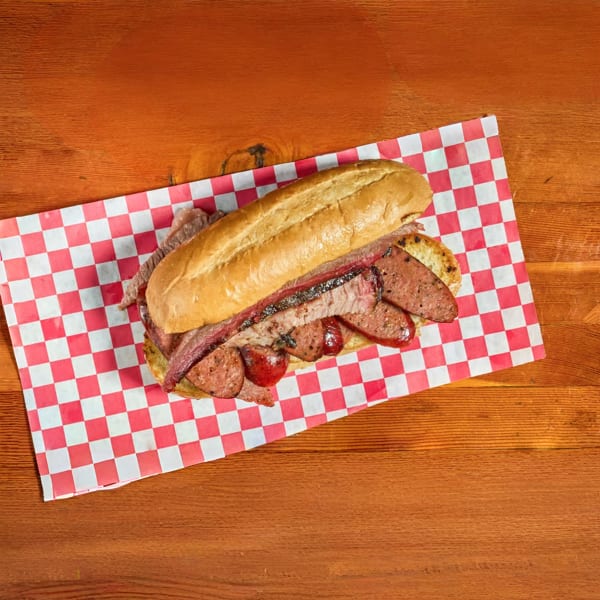 A large BBQ sandwich with brisket and sausage on a red and white checkered paper.