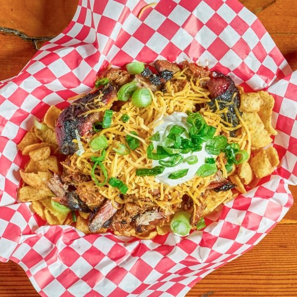 BBQ nachos with pulled pork, brisket, shredded cheese, sour cream, and green onions in a red checkered basket.