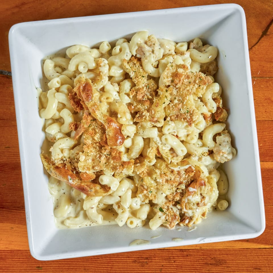 A white square bowl filled with creamy macaroni and cheese topped with crispy breadcrumbs on a wooden table.