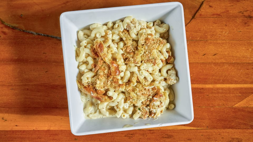 A white square bowl filled with creamy macaroni and cheese topped with crispy breadcrumbs on a wooden table.