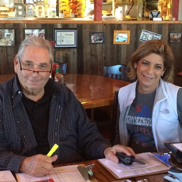 Two smiling people, a man and a woman, seated at a wooden table in a rustic restaurant.